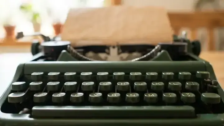 Close-up of the keys of an old forest-green manual typewriter with a sheet of kraft paper rolled in, morning light behind, slow camera move